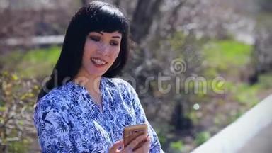美丽的亚洲女孩<strong>坐在</strong>长凳上的<strong>公园里</strong>，在智能手机上写一条信息
